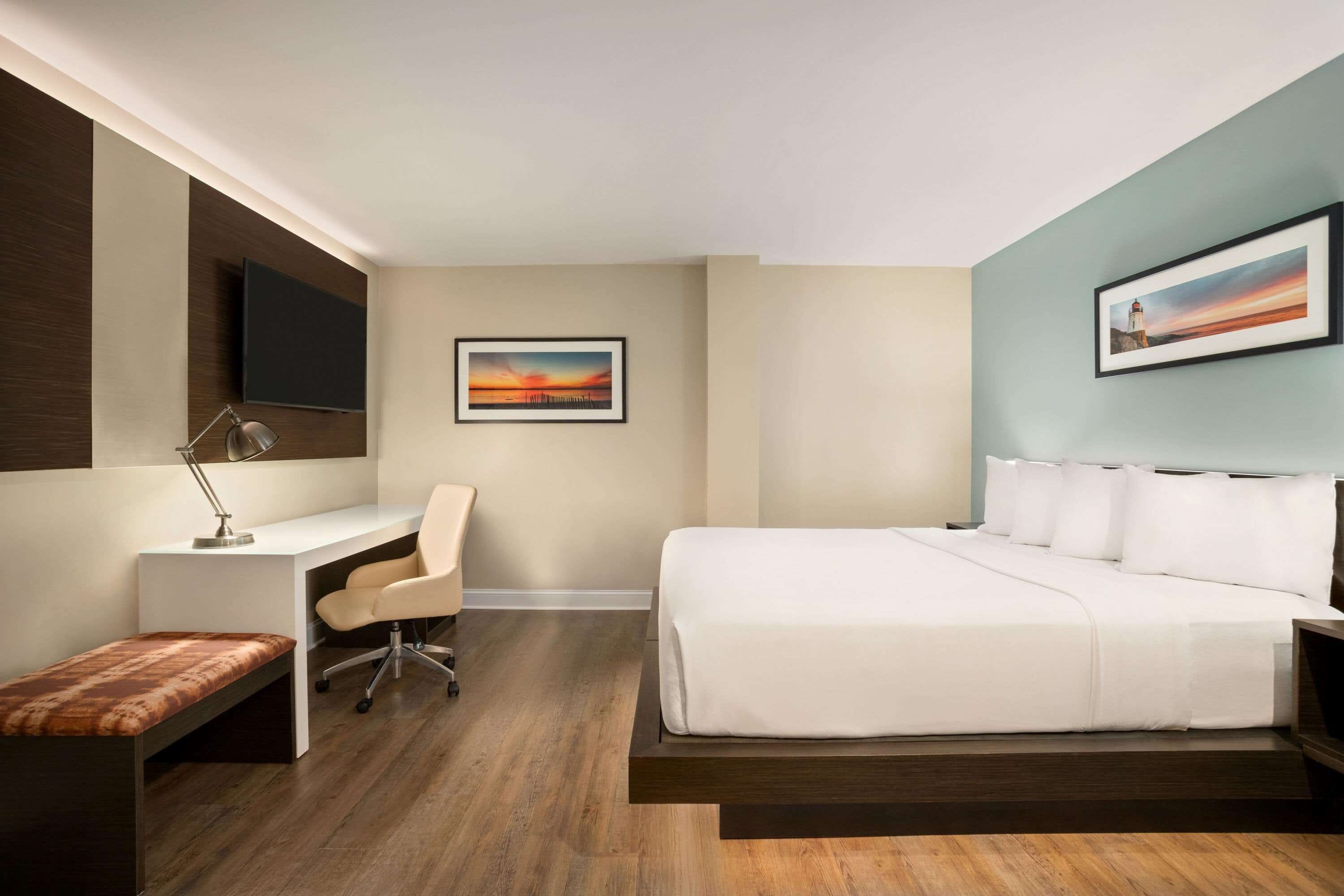 A modern hotel room with a bed, desk, chair, and a TV mounted on the wall.
