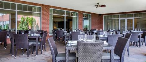 An outdoor patio area with multiple tables and chairs, large windows, and ceiling fans.