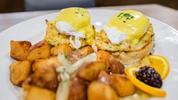 Ein Teller mit Eggs Benedict, Kartoffelrösti und einer Orangenscheibe.