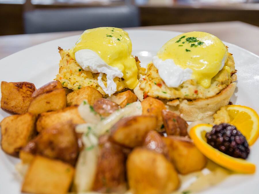 Ein Teller mit Eggs Benedict, Kartoffelrösti und einer Orangenscheibe.