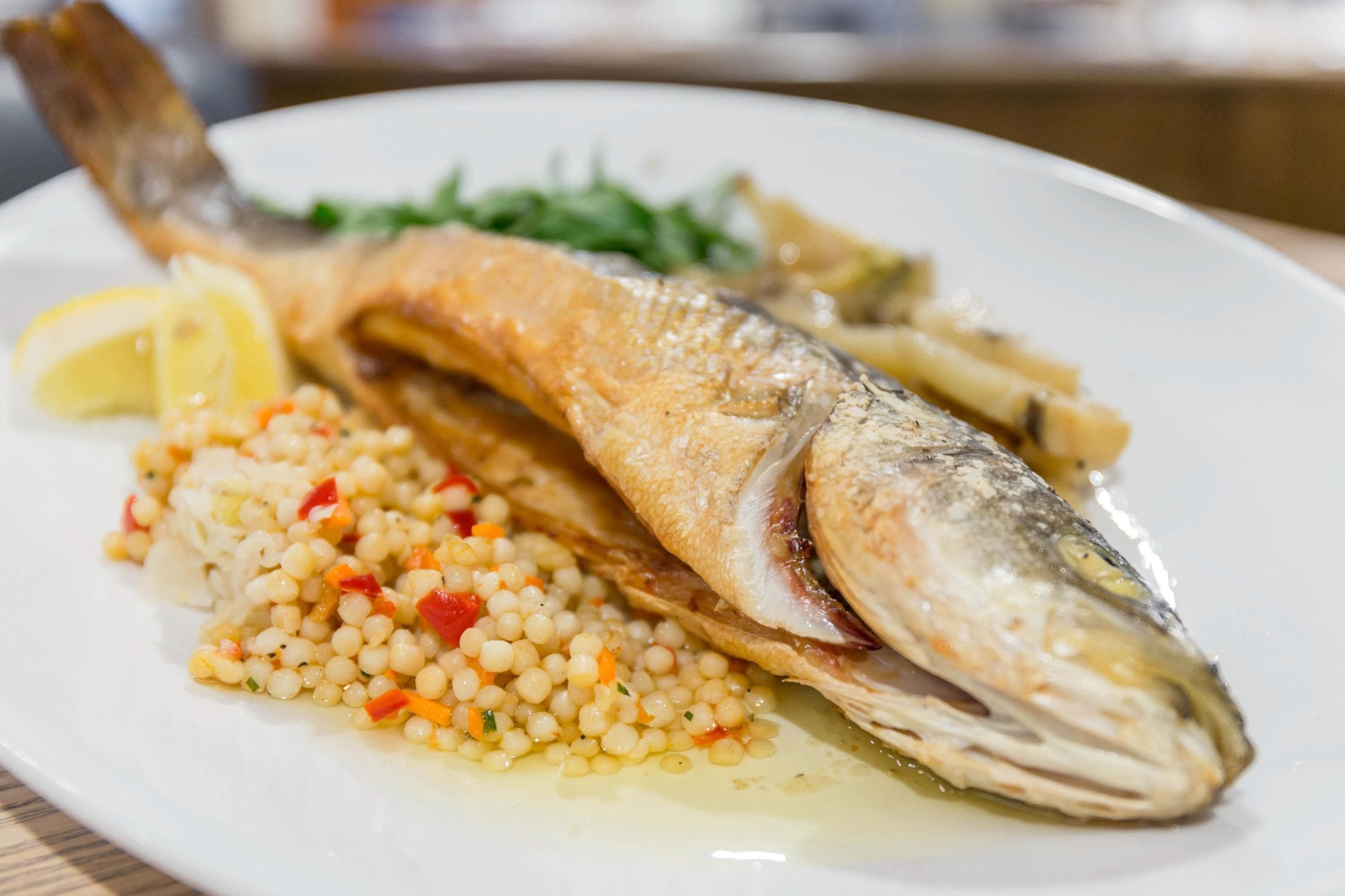 A plate with a whole fish, lemon, and a side of couscous.