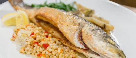 Ein Teller mit einem ganzen Fisch, einer Zitrone und einer Portion Couscous.