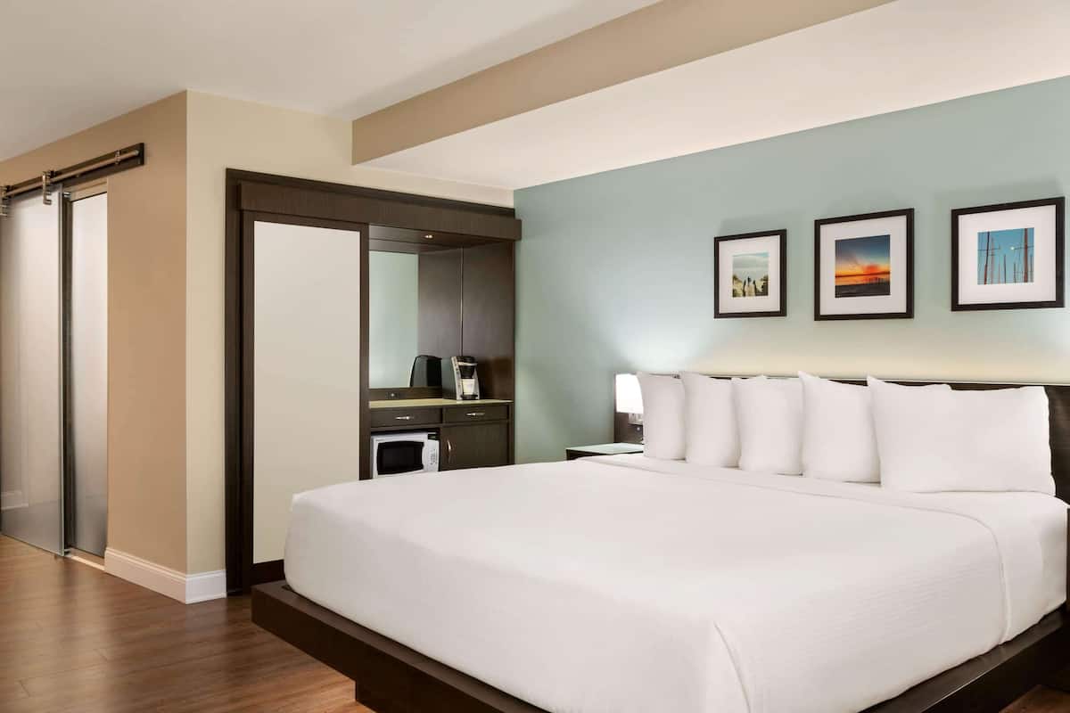 Une chambre d’hôtel avec un grand lit, un bureau avec une chaise, un miroir et une armoire. Trois tableaux encadrés sont accrochés au mur.