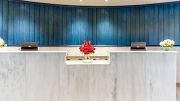 A reception desk with two laptops, a vase of red flowers, and a blue paneled wall.