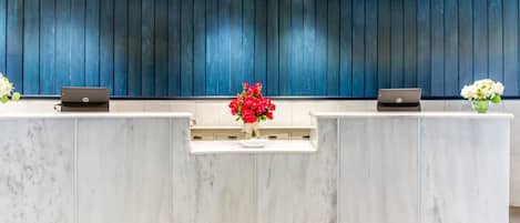 A reception desk with two laptops, a vase of red flowers, and a blue paneled wall.