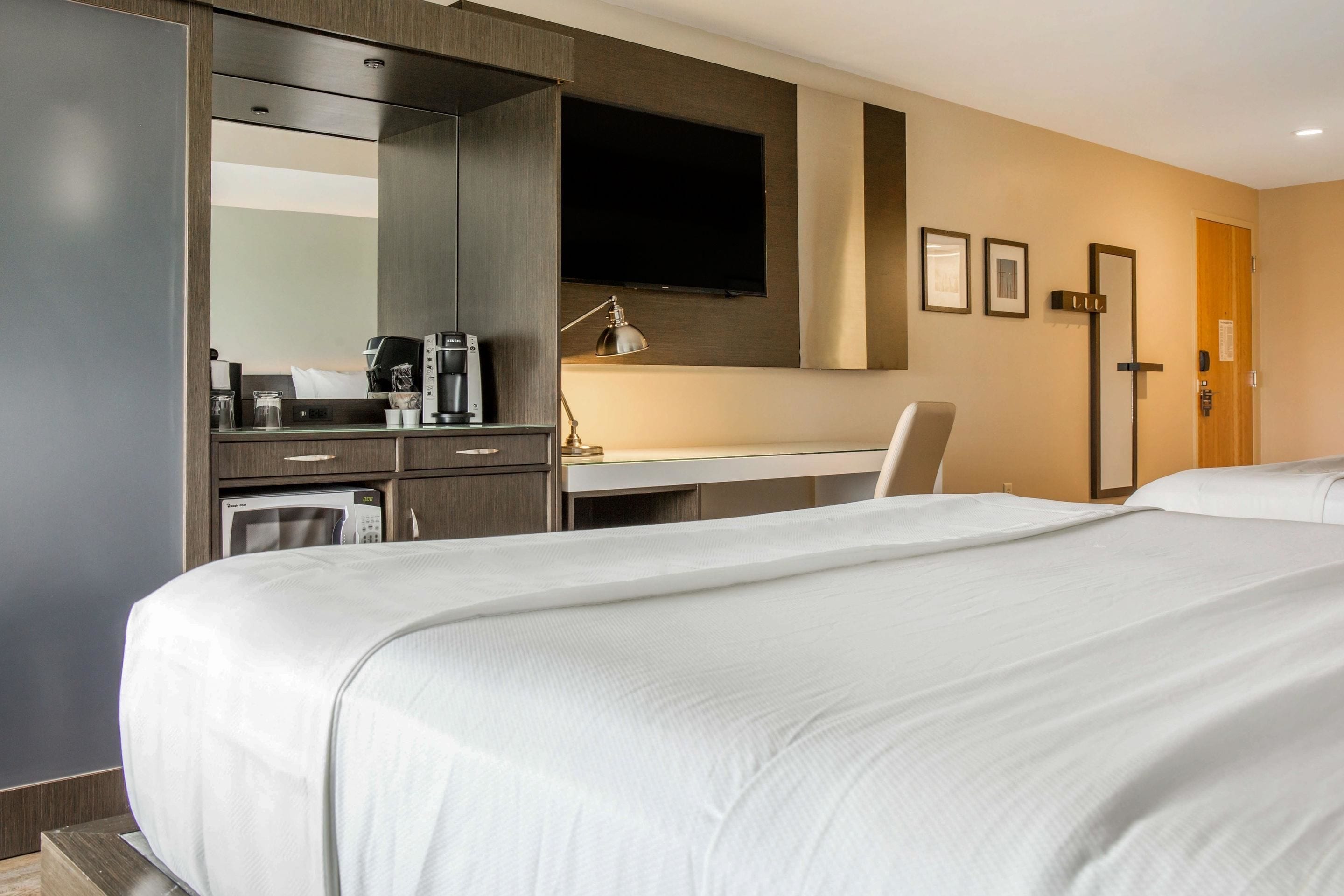 A hotel room with a large bed, a desk with a chair, a flat-screen TV, a coffee maker, and a microwave.