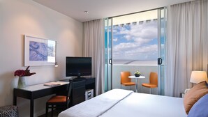 Habitación de hotel con cama, escritorio, computadora, dos sillas, una mesita y ventana con cortinas.