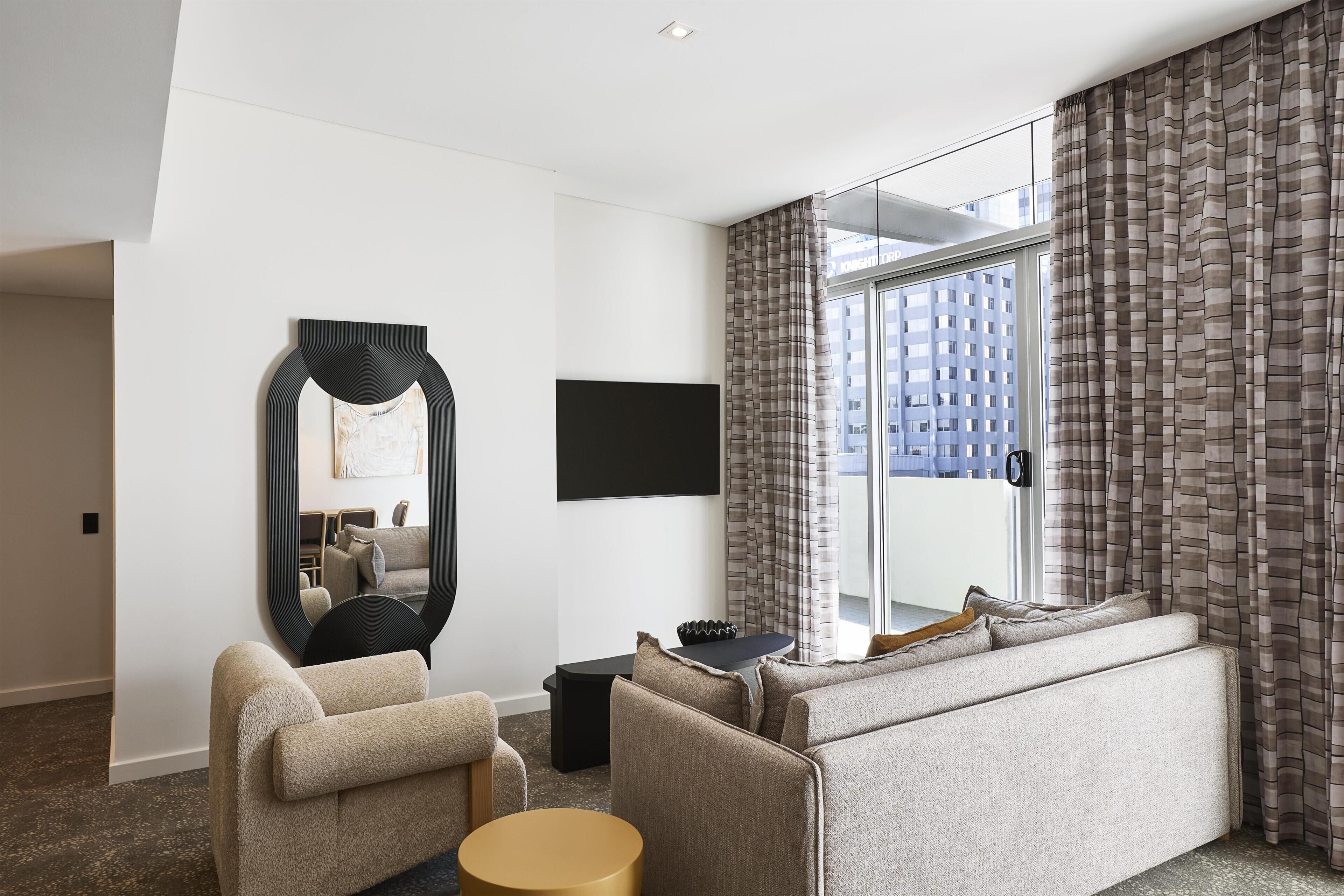 Une chambre d’hôtel moderne équipée d’un canapé, d’un fauteuil, d’une table ronde et d’un grand miroir.