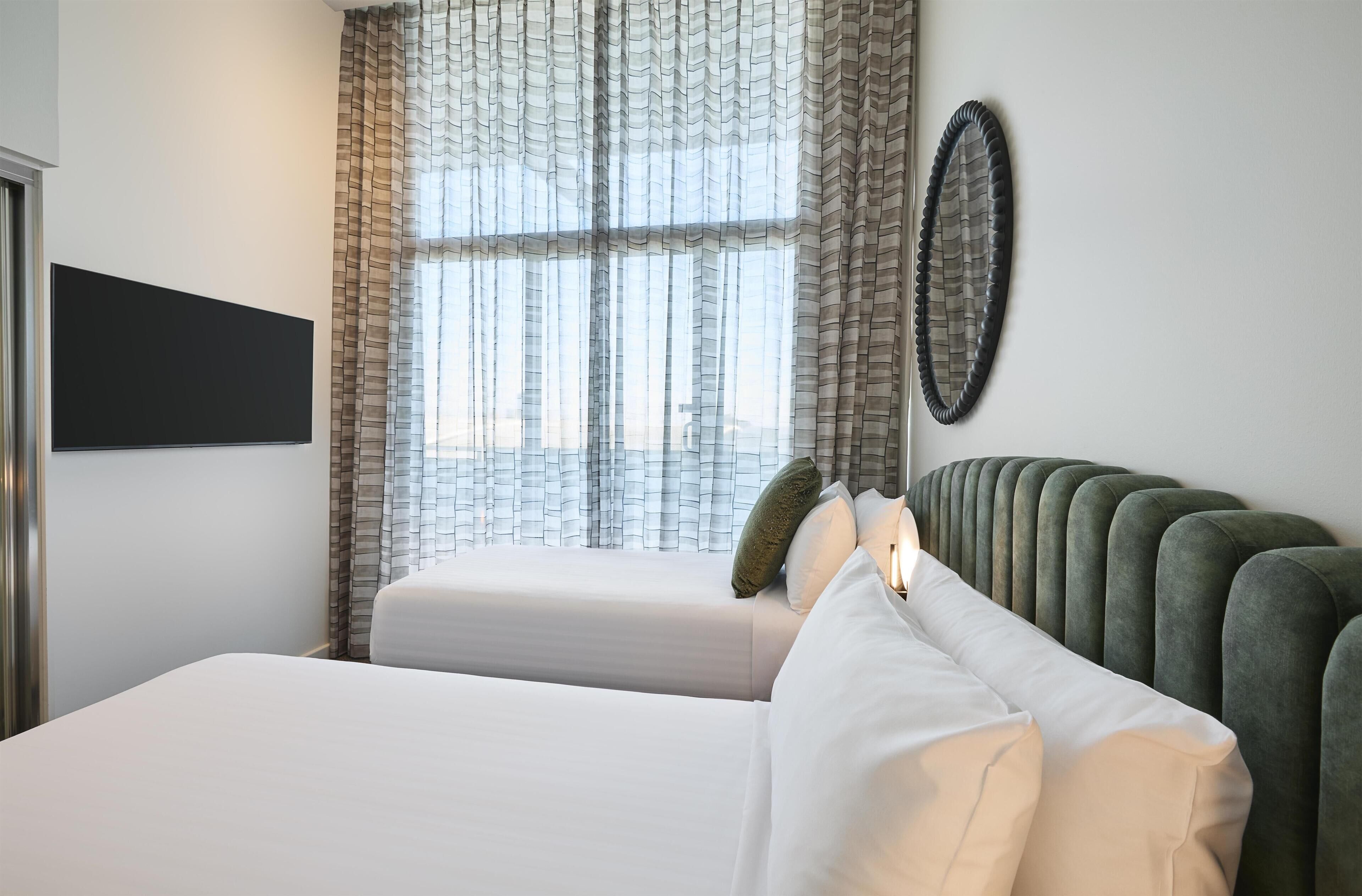 A hotel room with a bed, a television mounted on the wall, and a window with curtains.