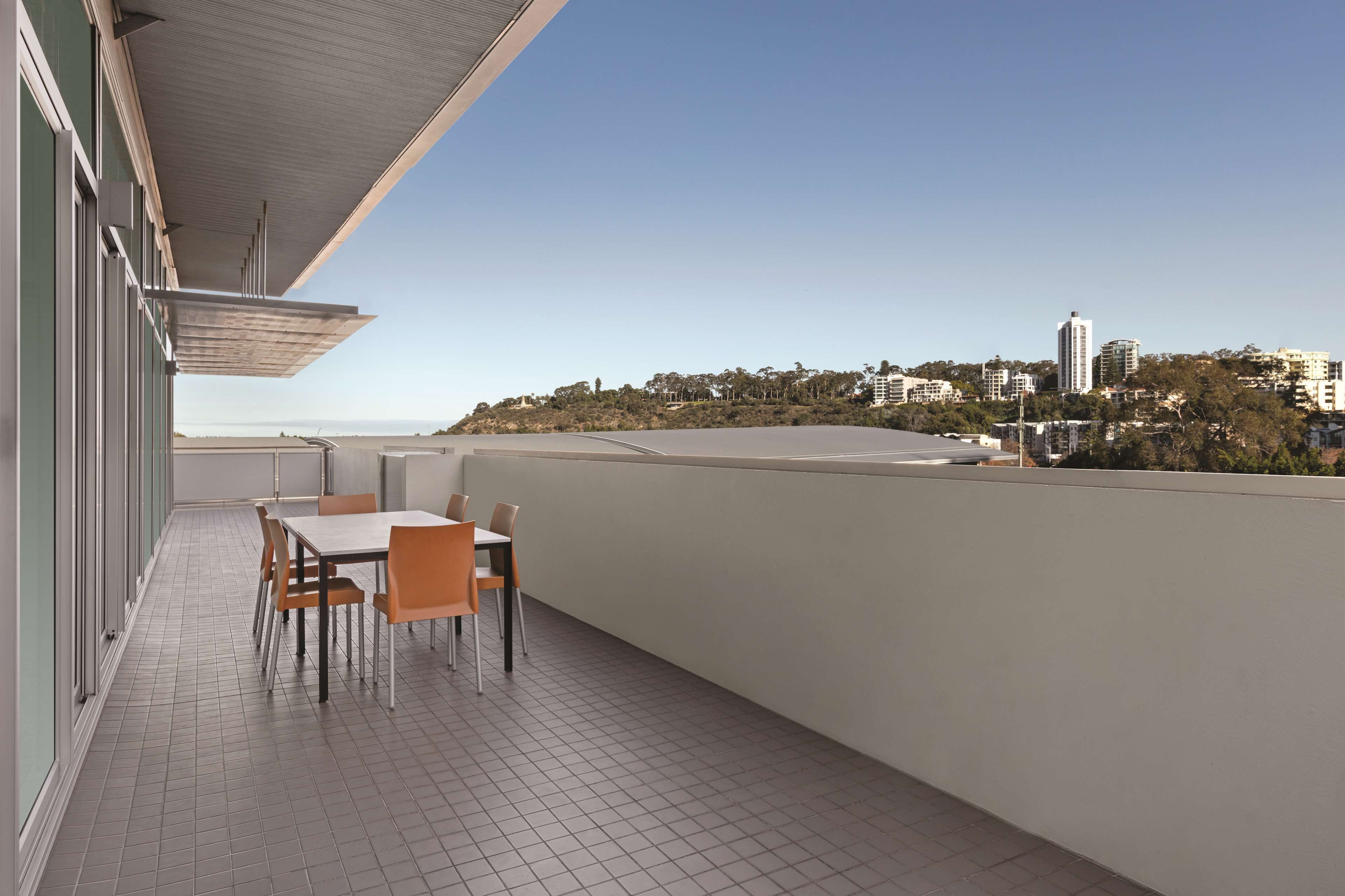 A balcony with a table and chairs, a view of a cityscape, and a tiled floor.