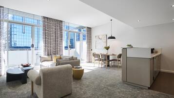 A modern hotel room with a living area, a dining table, and a kitchenette.