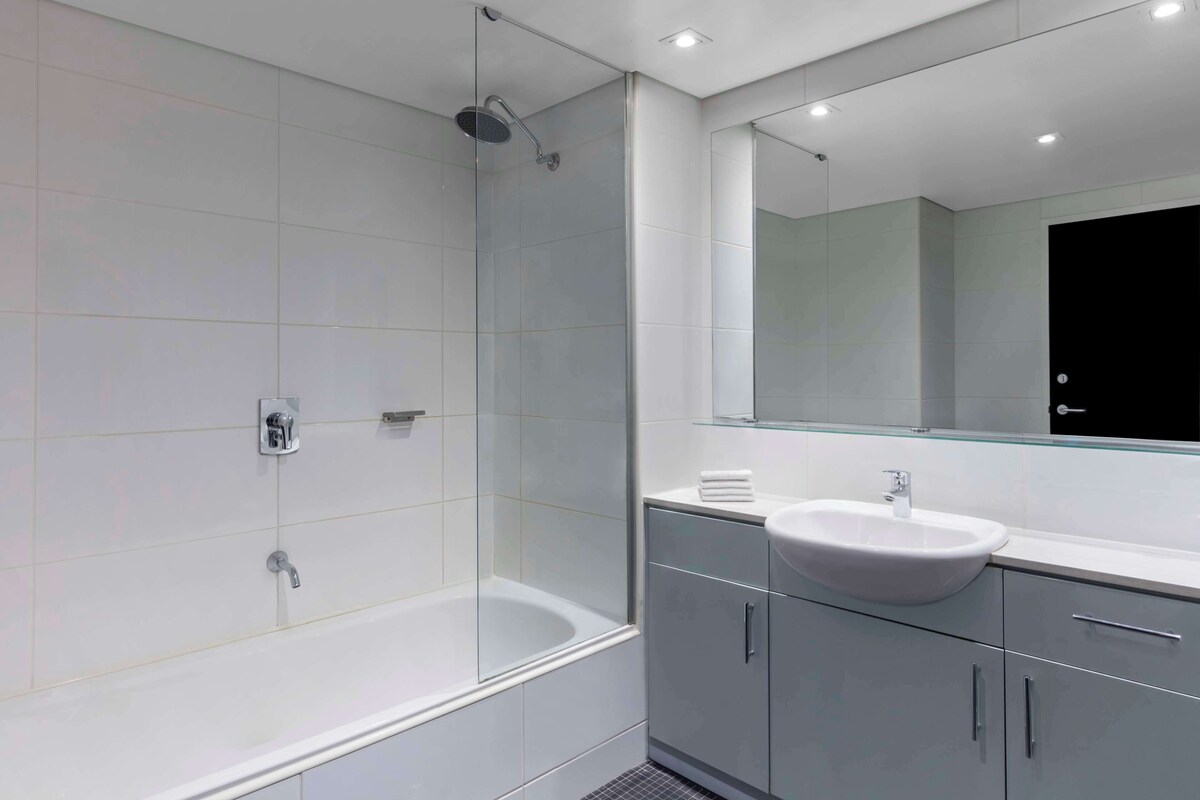 Un baño moderno con ducha de vidrio, lavamanos blanco y un espejo grande.