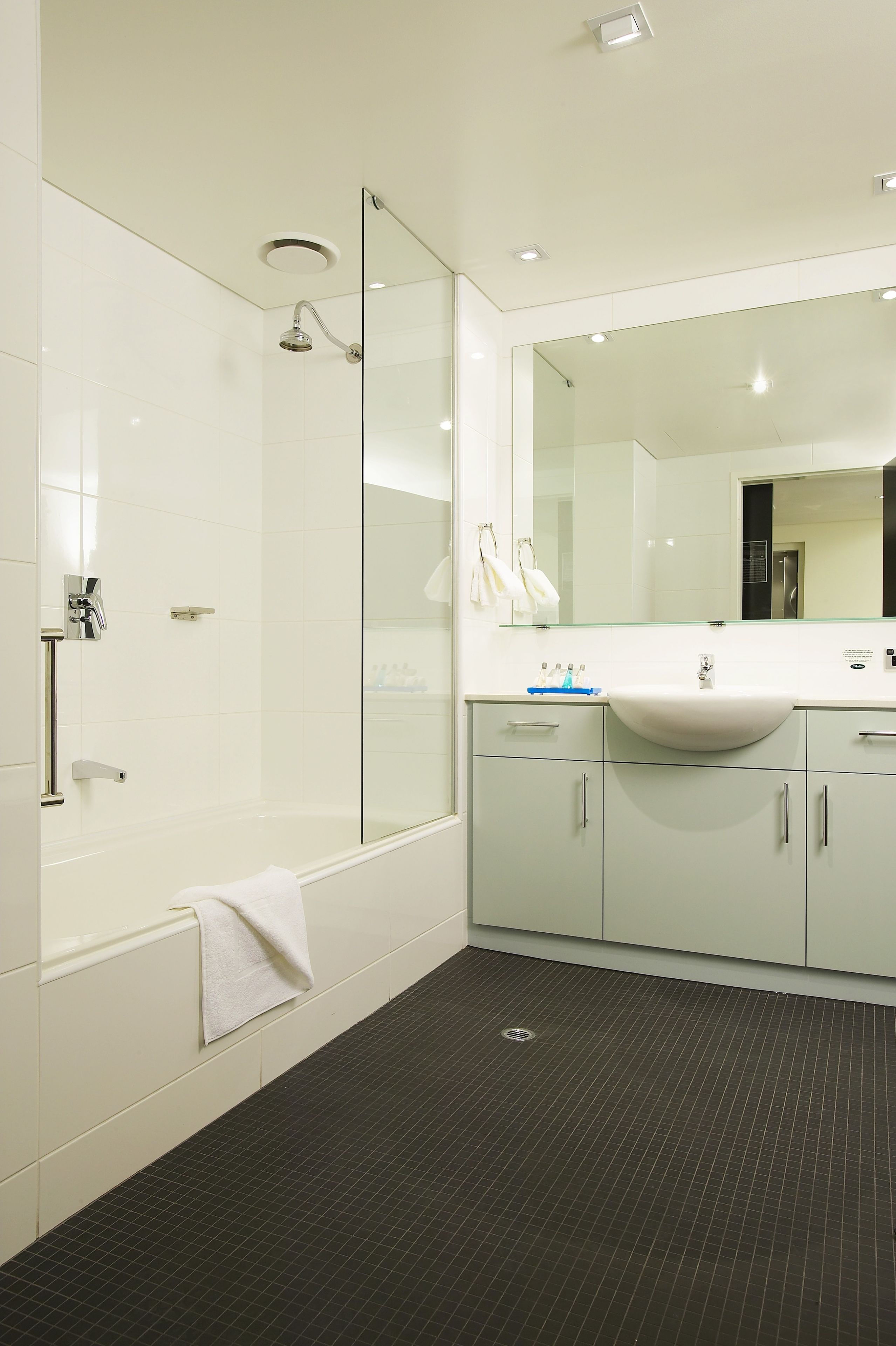 A modern bathroom with a glass-enclosed shower, a large mirror, and a white sink.