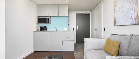 A modern living room with a grey sofa, a coffee table, and a kitchen area with white cabinets and a blue countertop.