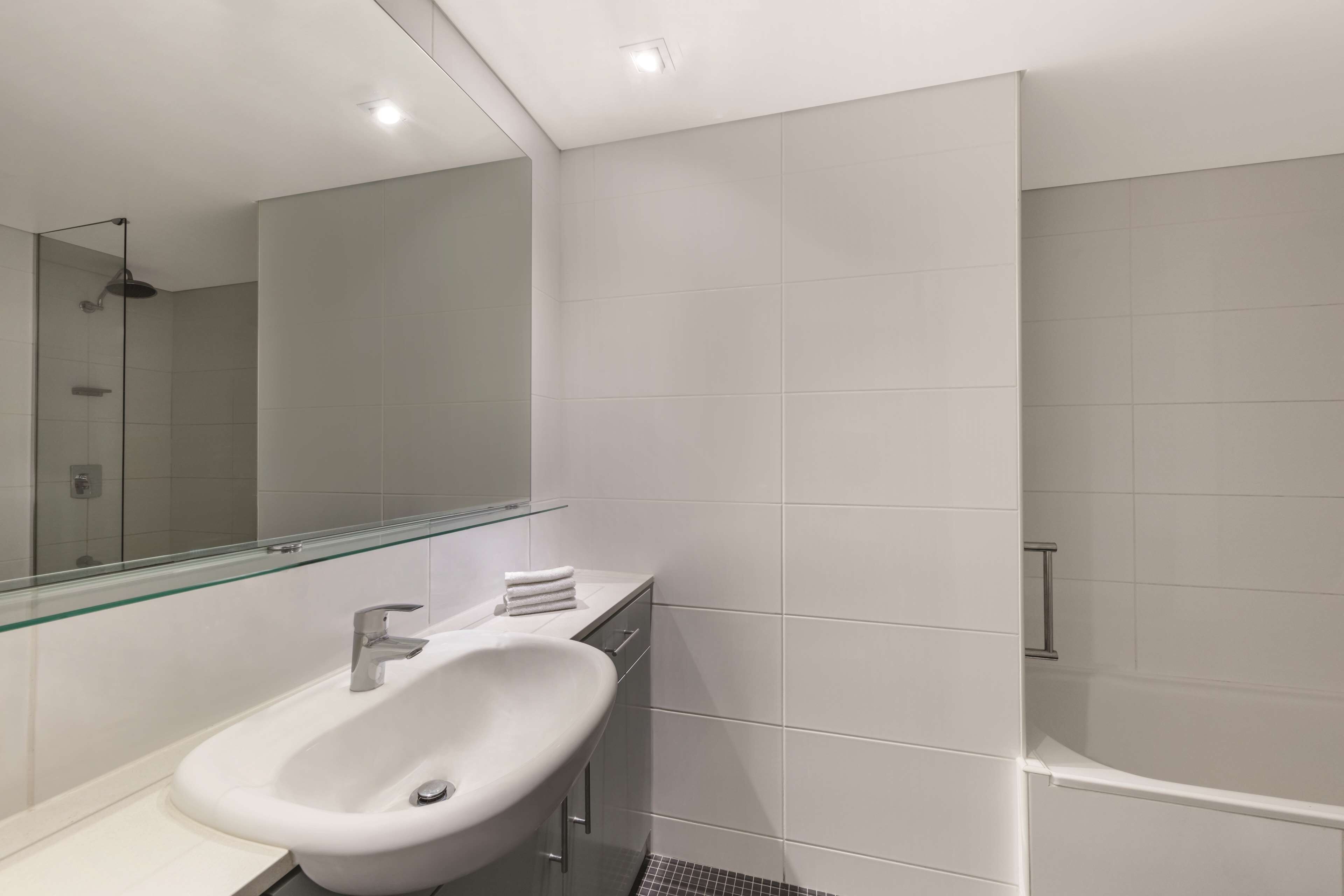A modern bathroom with a glass shower enclosure, a white sink, and a large mirror.