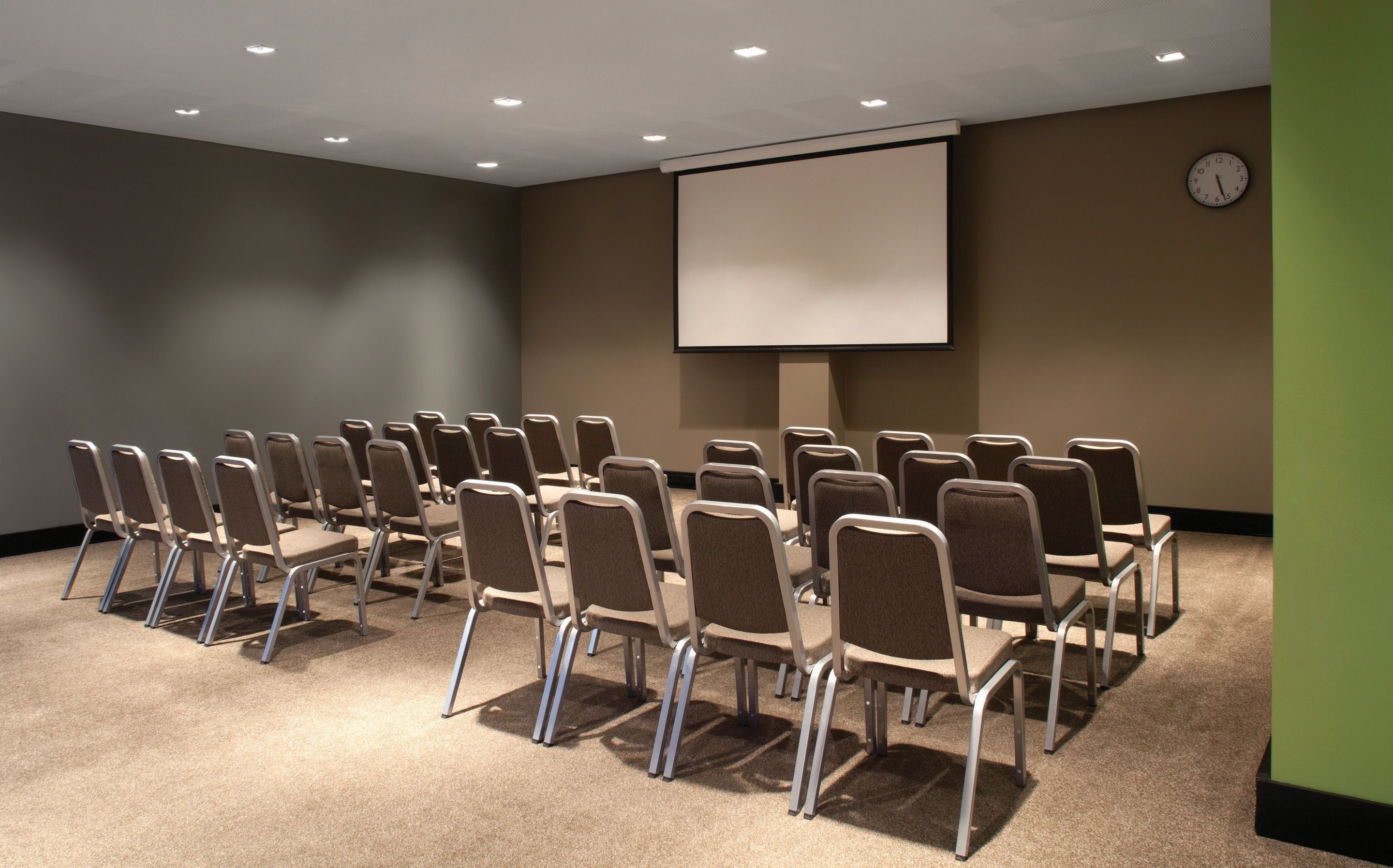Ein Konferenzraum mit Reihen von Stühlen, einer Projektionsleinwand und einer Uhr an der Wand.