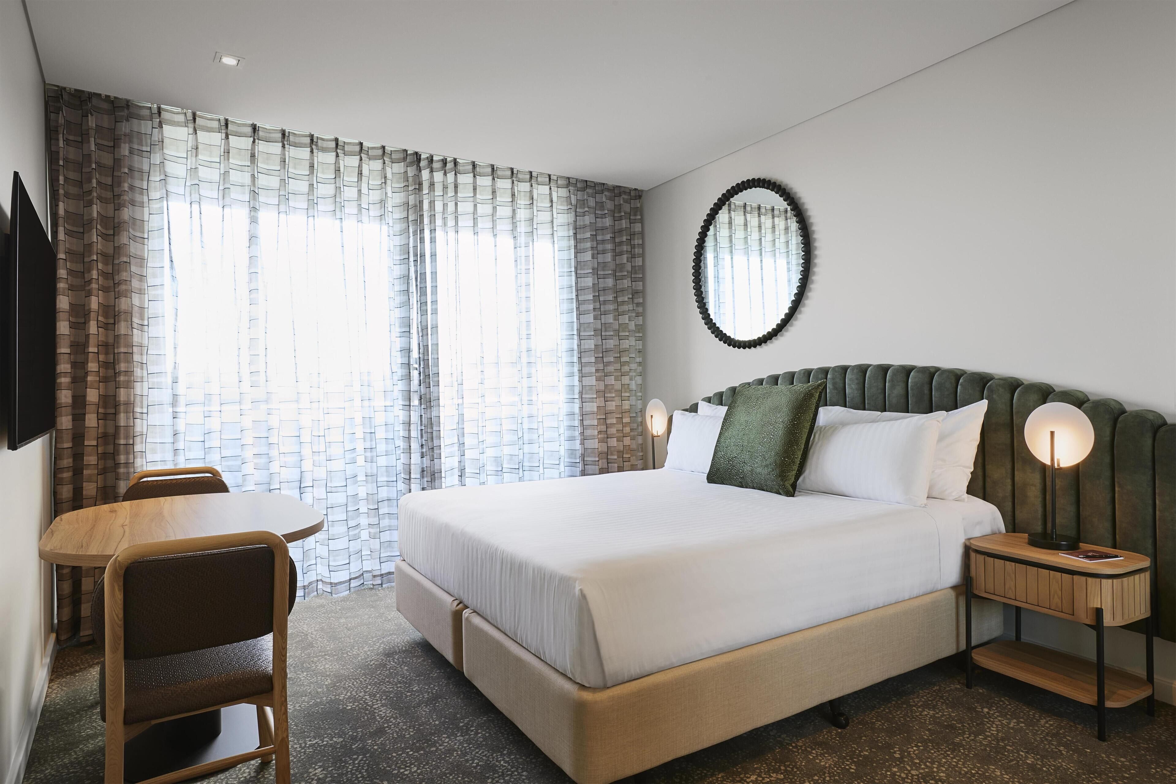 A hotel room with a bed, bedside tables, a chair, a mirror, and curtains.