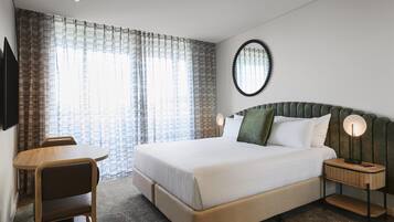 A hotel room with a bed, bedside tables, a chair, a mirror, and curtains.