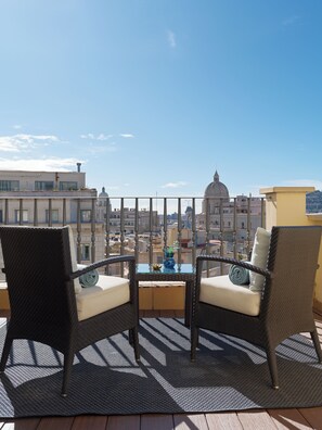 Un balcon avec des fauteuils en osier, une petite table et un vase de fleurs.