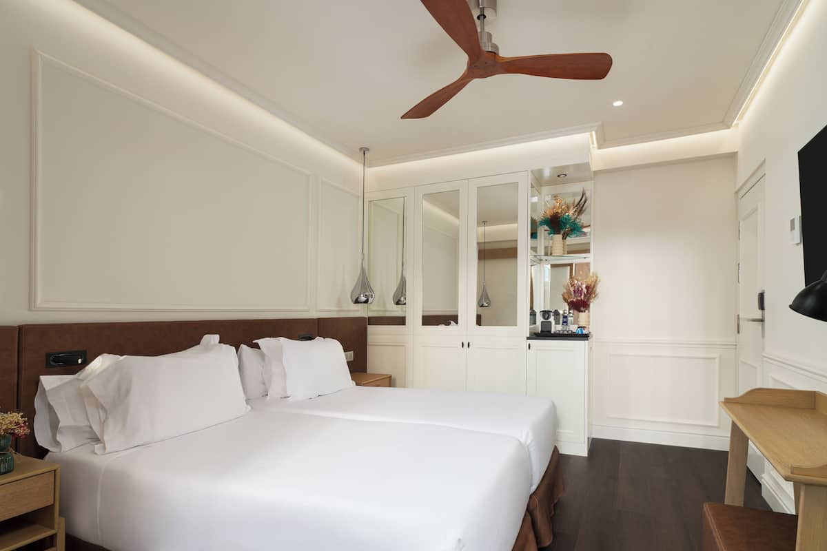 Een hotelkamer met een groot bed, een plafondventilator, een bureau en een spiegel.