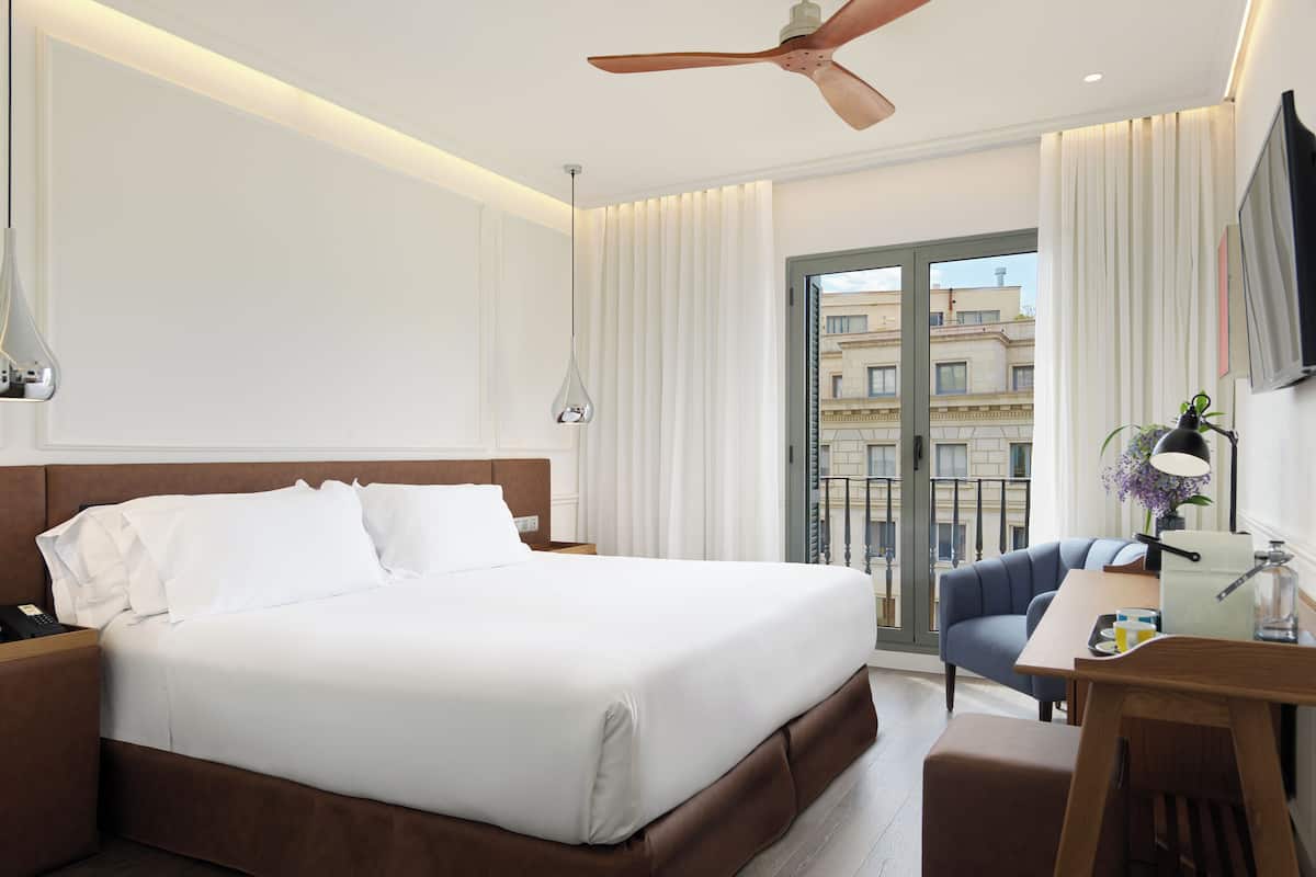 Een moderne hotelkamer met een groot bed, een bureau, een stoel, een plafondventilator en uitzicht op de stad door het raam.