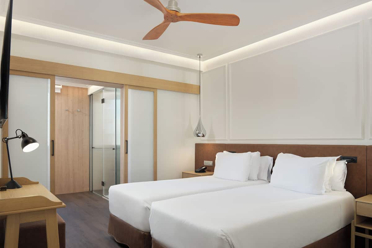 Hotelkamer met een bed, nachtkastjes, bureau, lamp, plafondventilator en een deur naar een andere kamer.