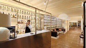 Et moderne barområde med bartender, hylder fyldt med spiritusflasker og et loungeområde med sofaer og borde.