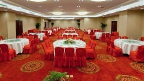 Un salón de banquetes con mesas redondas, sillas rojas y una alfombra roja.