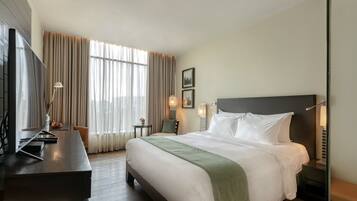 A hotel room with a large bed, a desk, a chair, a TV, and a window with curtains.