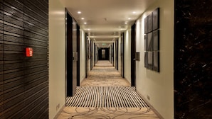 A hotel corridor with a patterned carpet, dark wooden paneling on one side, and framed artwork on the walls. - The Mirador Hotel, Mumbai International Airport (Mumbai)