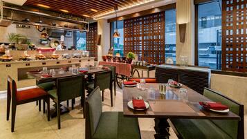 A restaurant with a modern interior, featuring wooden ceiling panels, large windows, and a view of the cityscape.