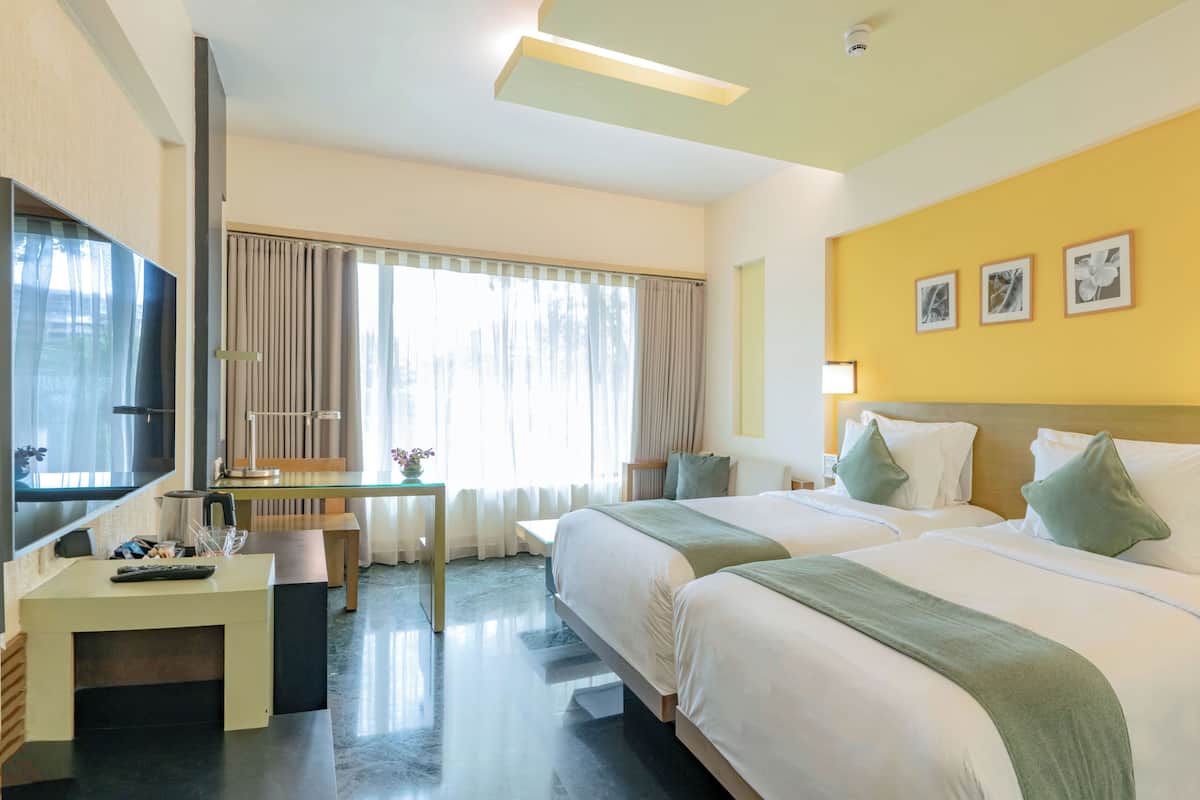 Habitación de hotel con dos camas, un escritorio, una silla, un televisor y una ventana con cortinas.