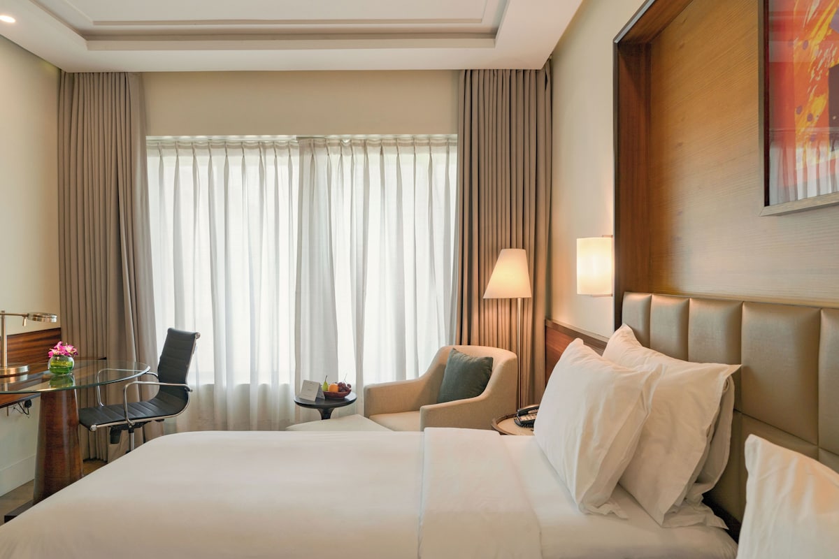 Habitación de hotel con cama, dos sillas, un escritorio con lámpara y una ventana con cortinas.