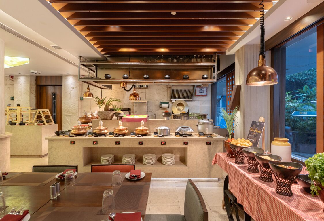 A modern dining area with a central buffet station, wooden ceiling, and large windows.