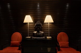 A room with a dark wooden wall, a Buddha statue, two red chairs, and two table lamps.