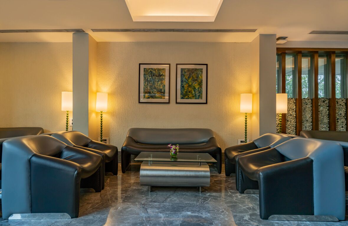 A modern lounge area with a sofa, two armchairs, and a coffee table. There are two framed abstract paintings on the wall and two floor lamps.