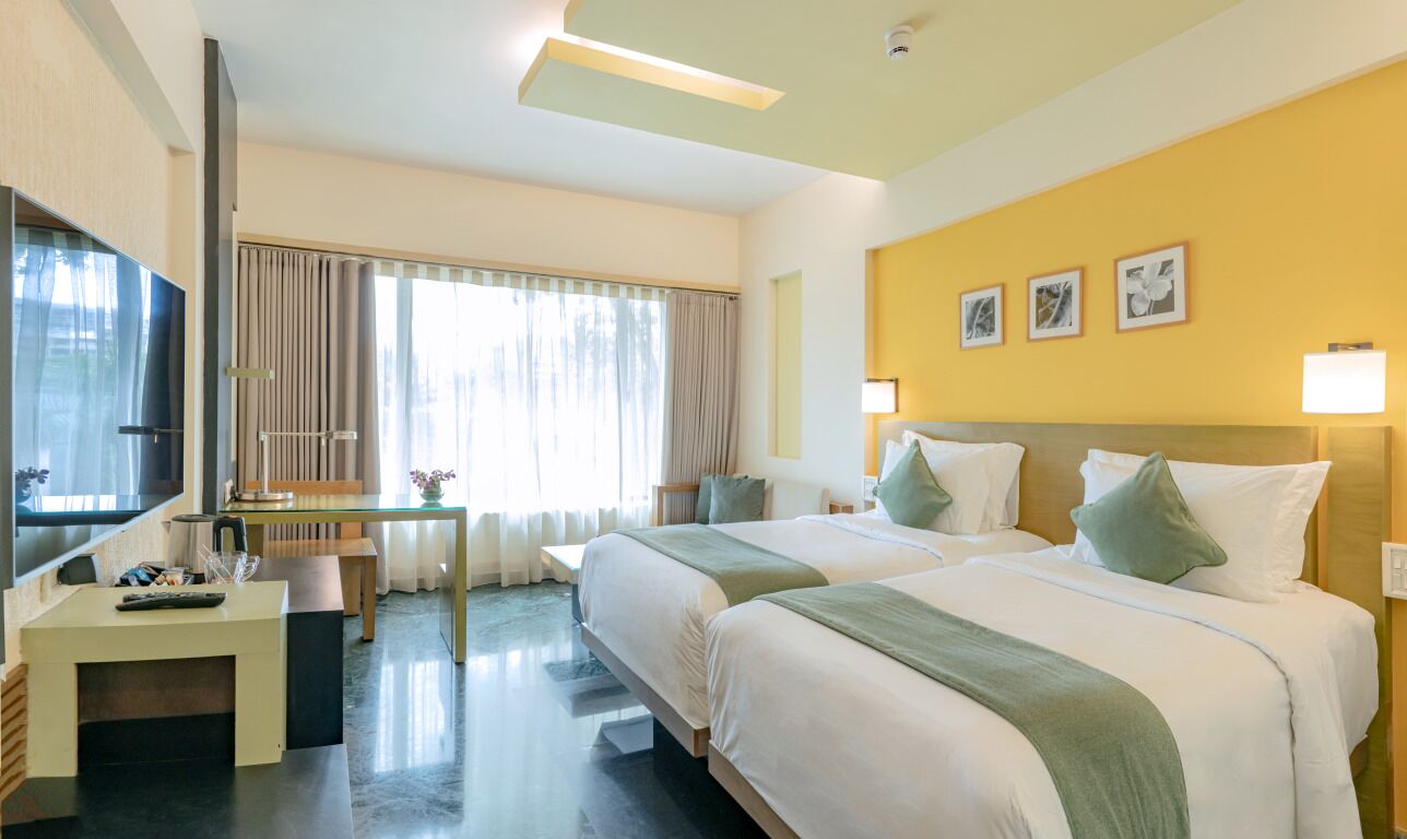 A hotel room with two beds, a desk, a TV, and a window with curtains.
