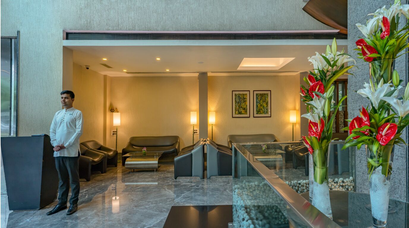 A hotel lobby with a reception desk, seating area, and decorative vases with flowers.