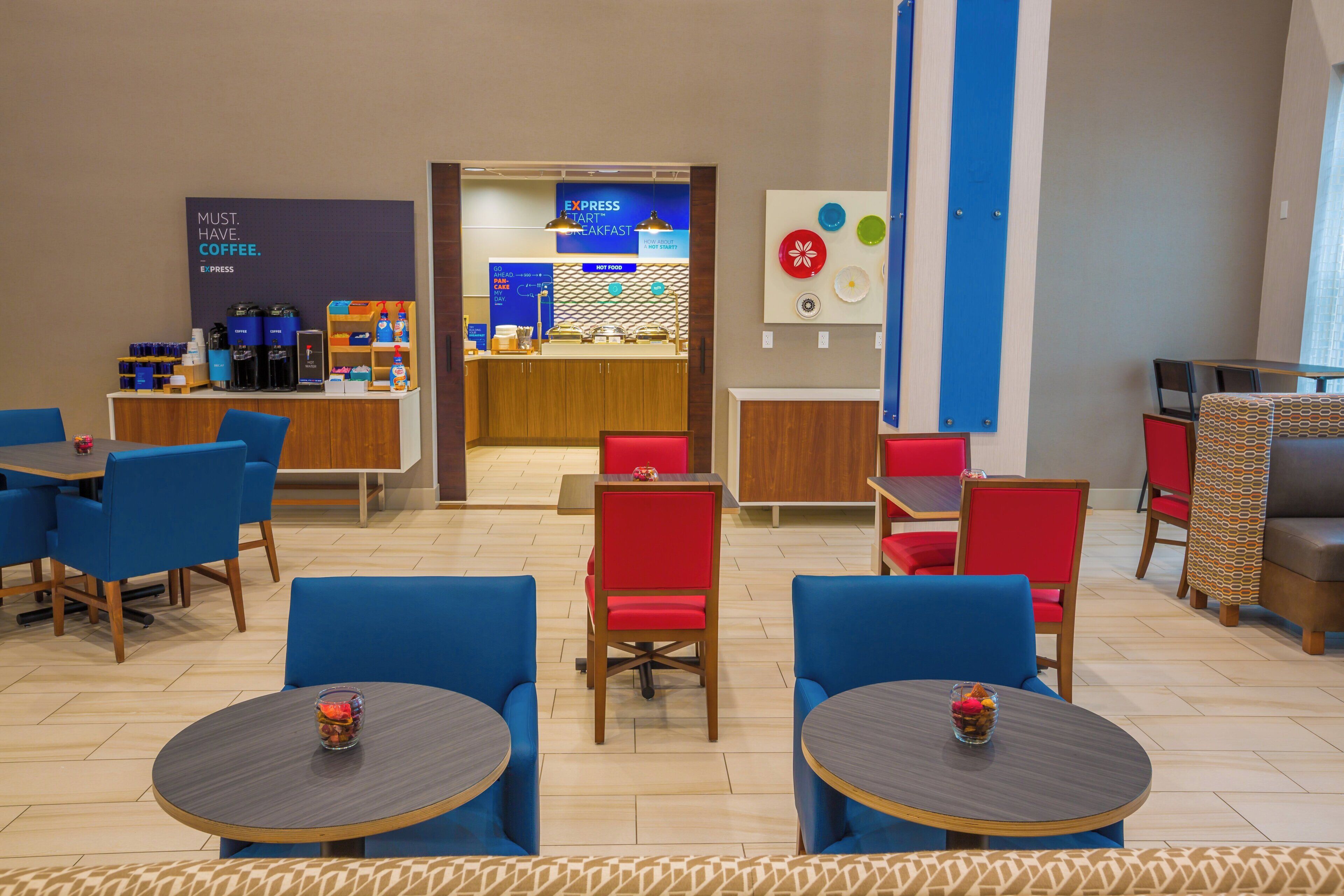 Un vestíbulo de hotel con zonas de estar, una estación de café y una barra de desayuno.
