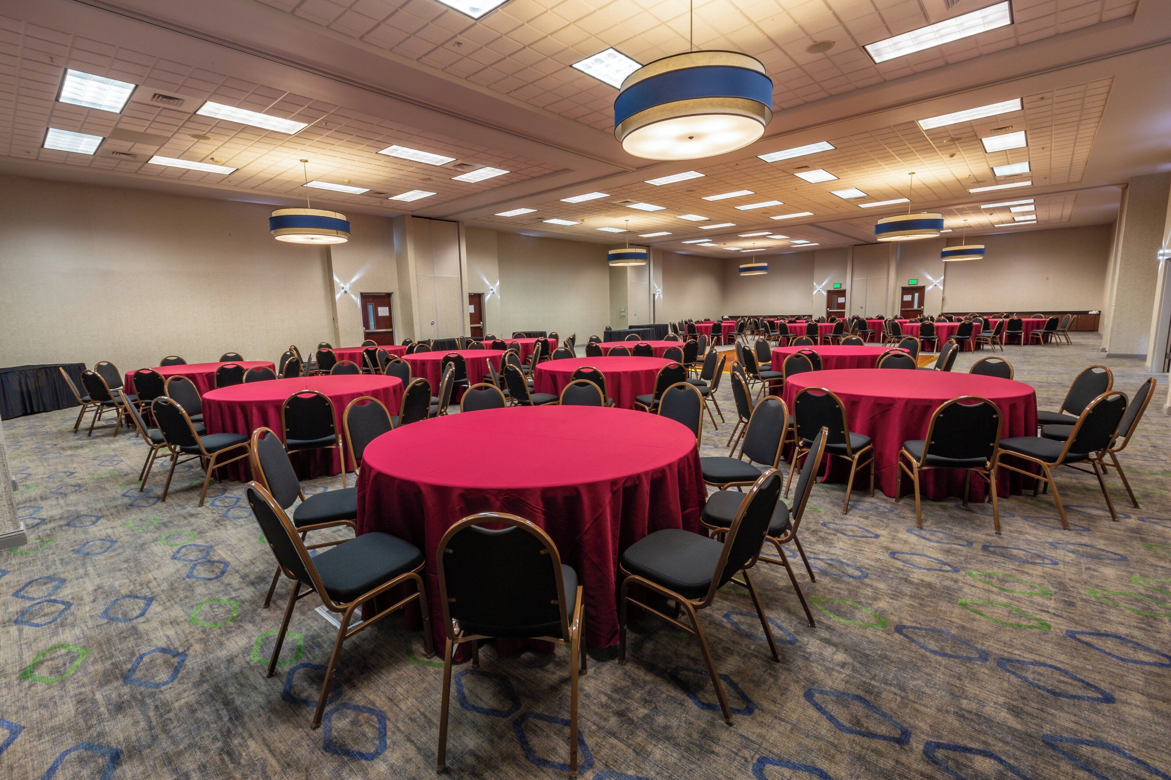 Une salle de conférence avec plusieurs tables rondes recouvertes de nappes rouges, disposées en rangées.