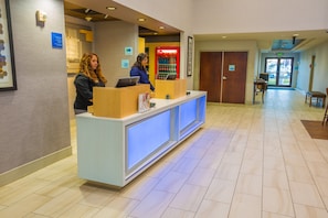 A reception area with a reception desk, two laptops, a refrigerator, and a door leading to the parking area.