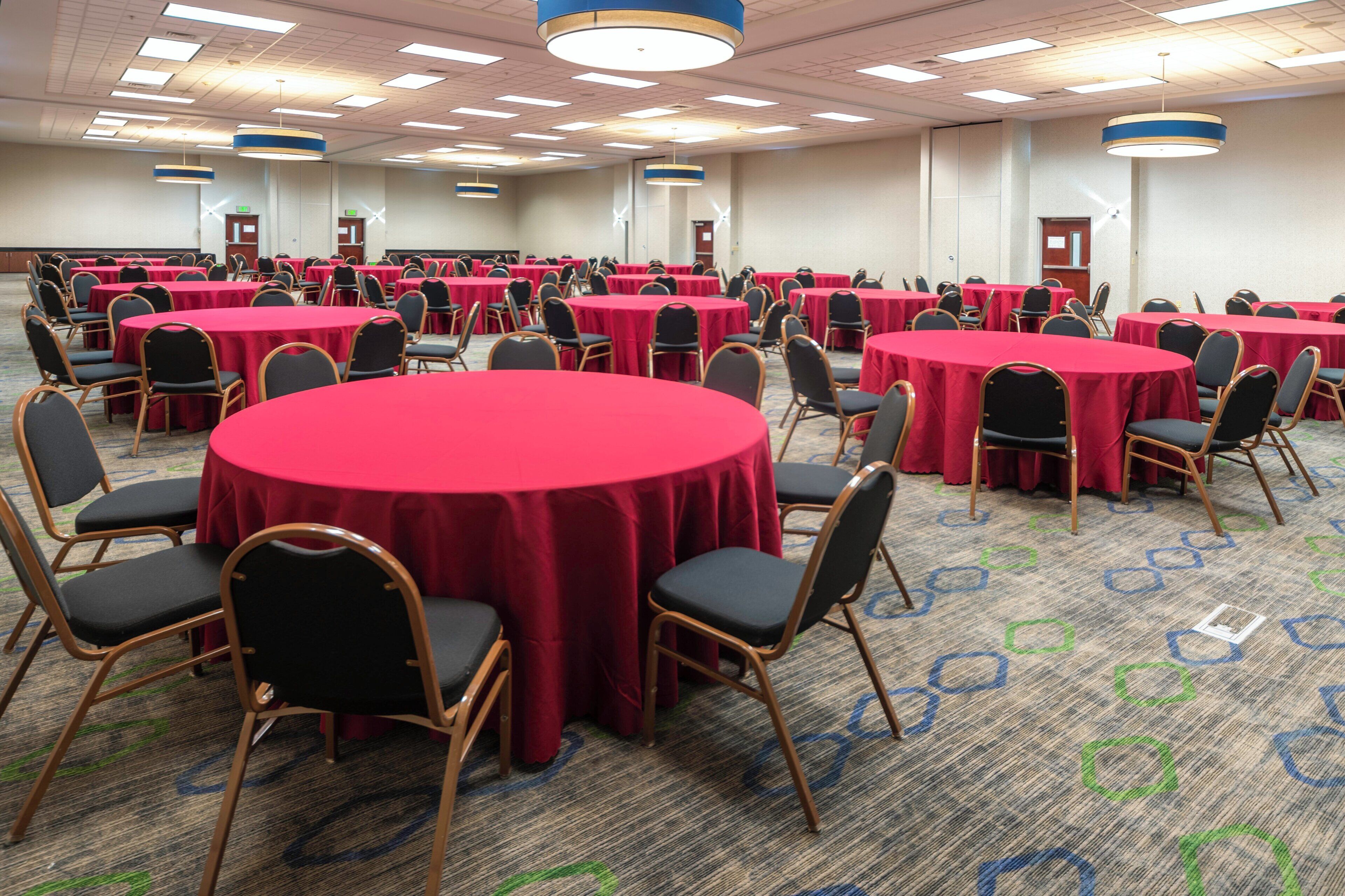 A conference room with multiple round tables covered with red tablecloths, black chairs, and overhead lighting.