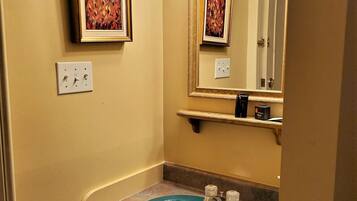 A bathroom with a blue sink, a mirror with lights, and a framed picture on the wall.
