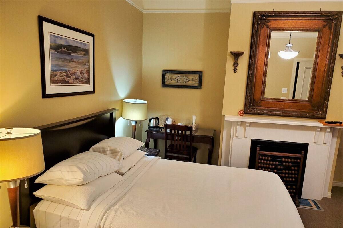 Een hotelkamer met een bed, een bureau, een stoel, een lamp, een open haard en een lijst aan de muur.