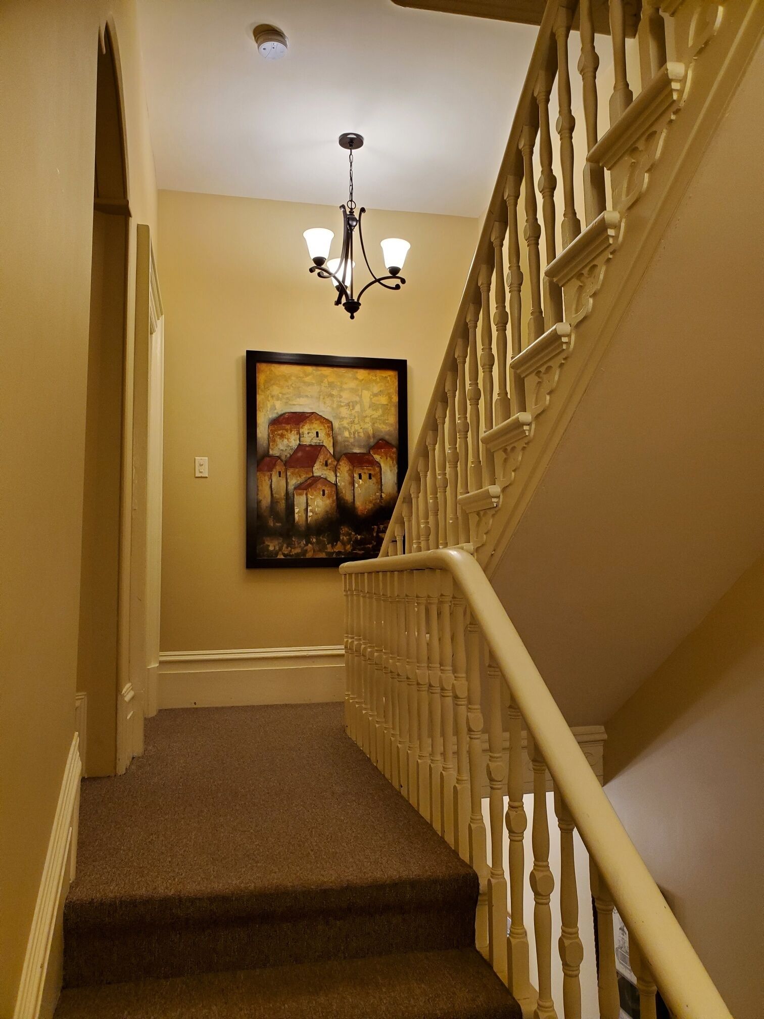 A carpeted staircase with a white balustrade, a chandelier, and a framed painting on the wall.