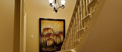 A carpeted staircase with a white balustrade, a chandelier, and a framed painting on the wall.