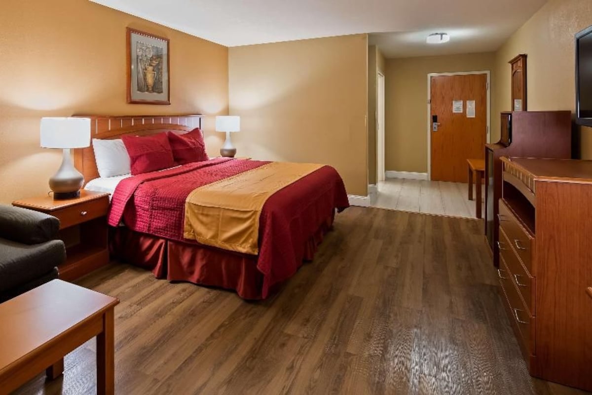 A hotel room with a bed, a desk, a chair, a television, and a door.
