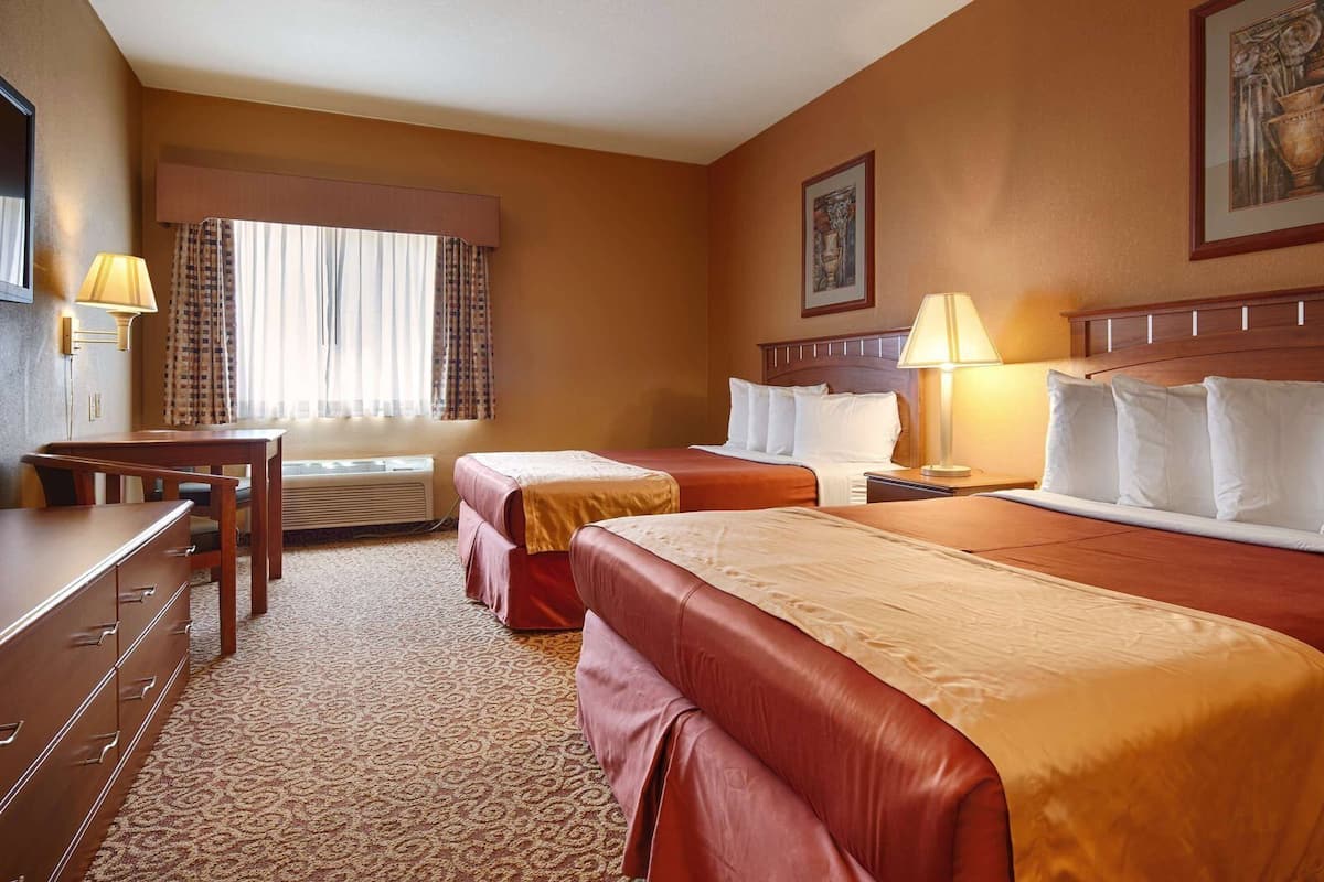 A hotel room with two beds, a desk, a chair, a lamp, and a painting on the wall.