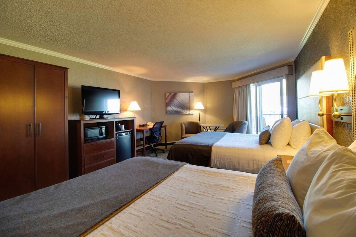 A hotel room with two beds, a desk, a television, and a window with curtains.