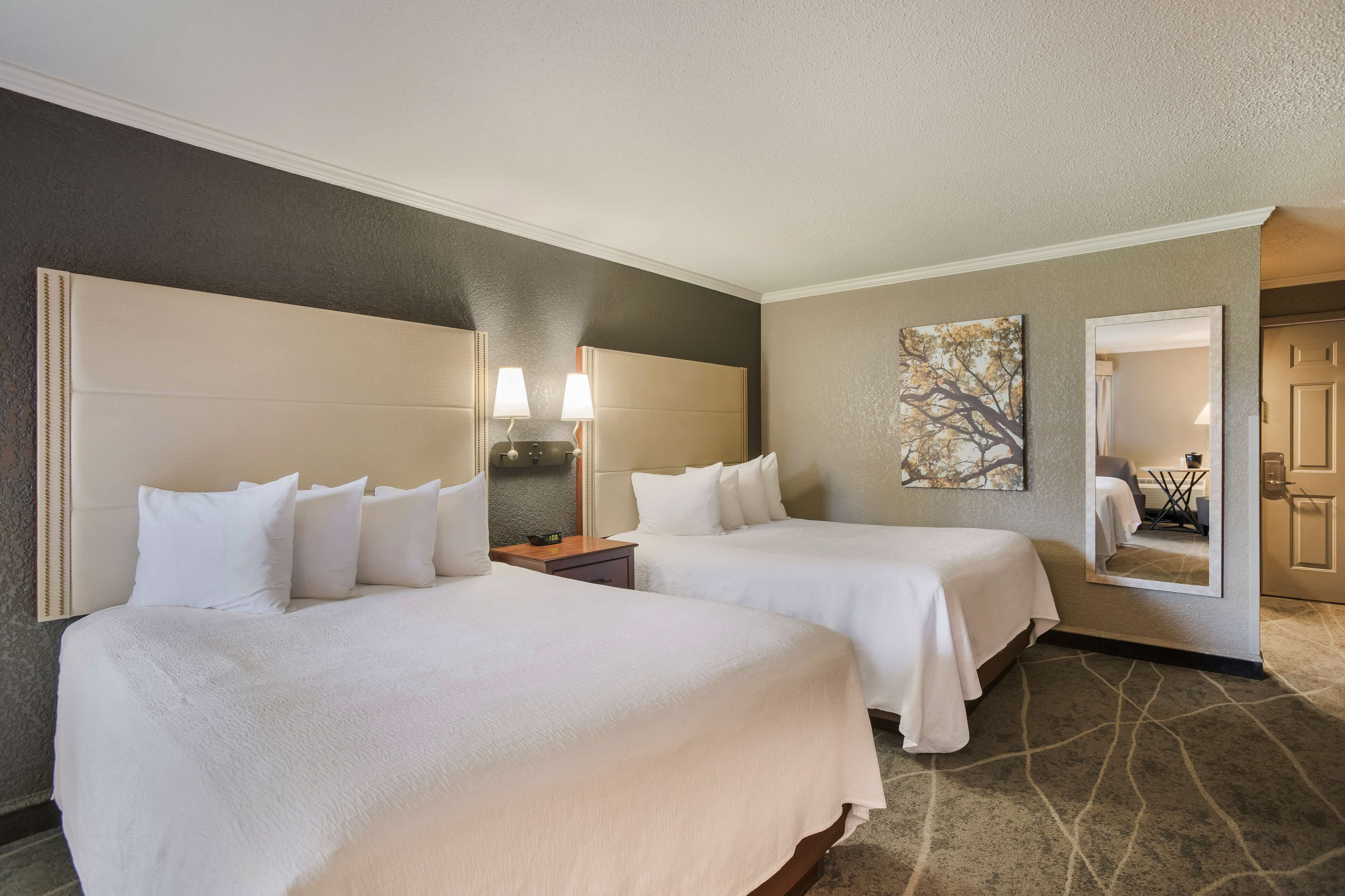 A hotel room with two beds, a large mirror, a painting, and a carpeted floor.